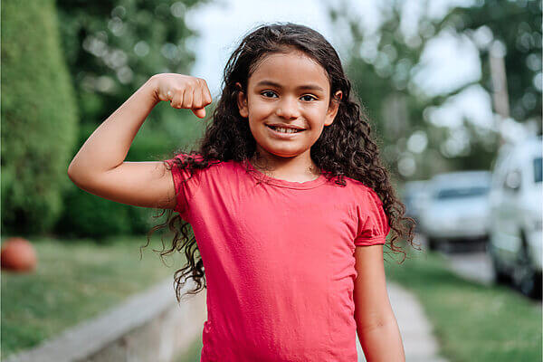 Young girl smiling at camera, flexing her muscles on one arm.